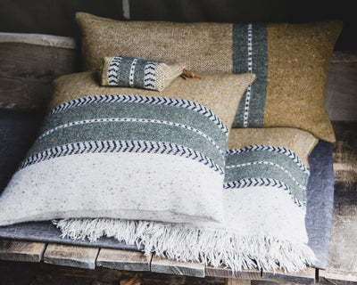 Three woven pillows and a small pouch with green and white striped patterns are arranged on a rustic wooden bench.