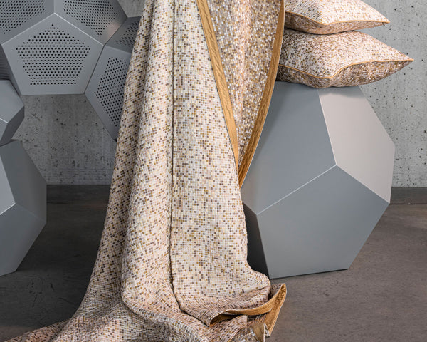 A beige and gold mosaic-patterned fabric drapes over geometric gray stools, with matching pillows placed on top.