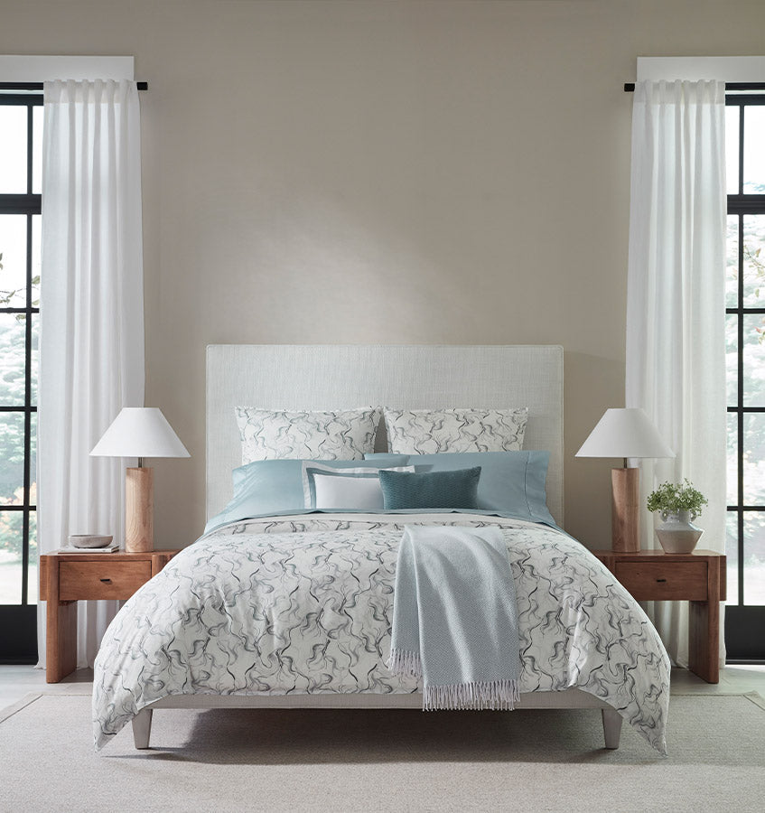 Sferra Muro bedding in ivory with grey marble print and dusty blue accent pillows on styled bed.
