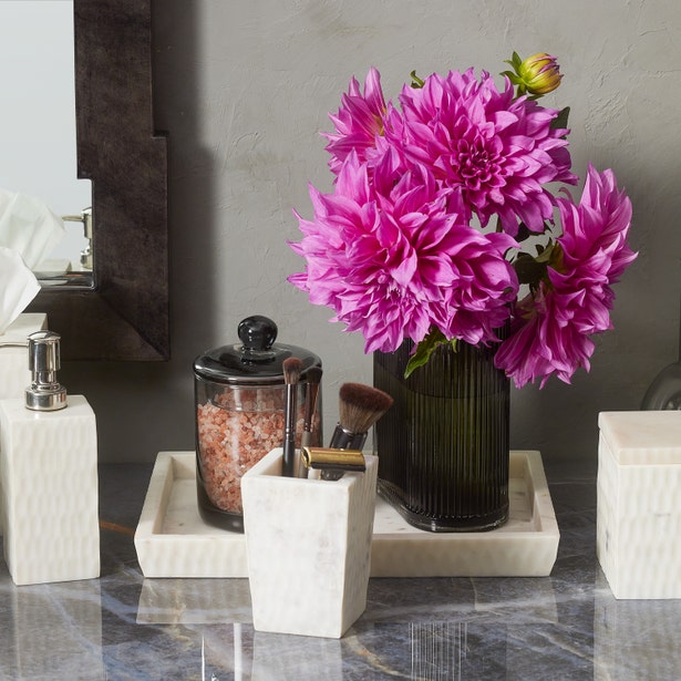Kuna bath accessories in white marble on a grey vanity with pink dahlia flowers.