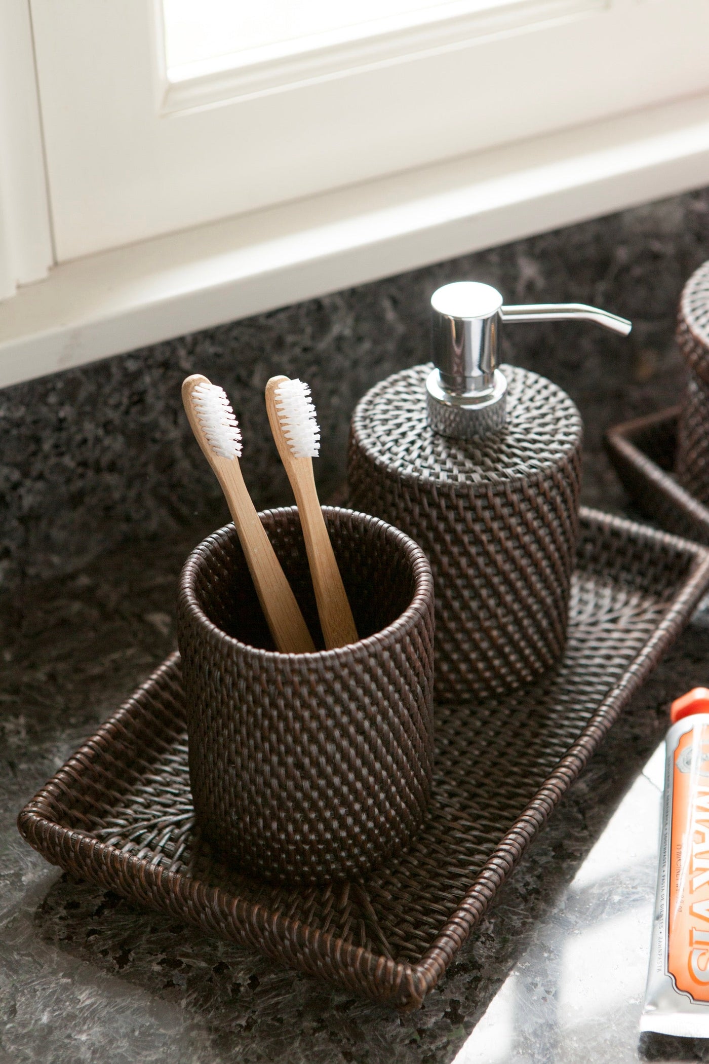 Dark rattan bathroom set with toothbrush holder, soap dispenser, and tray on granite counter.