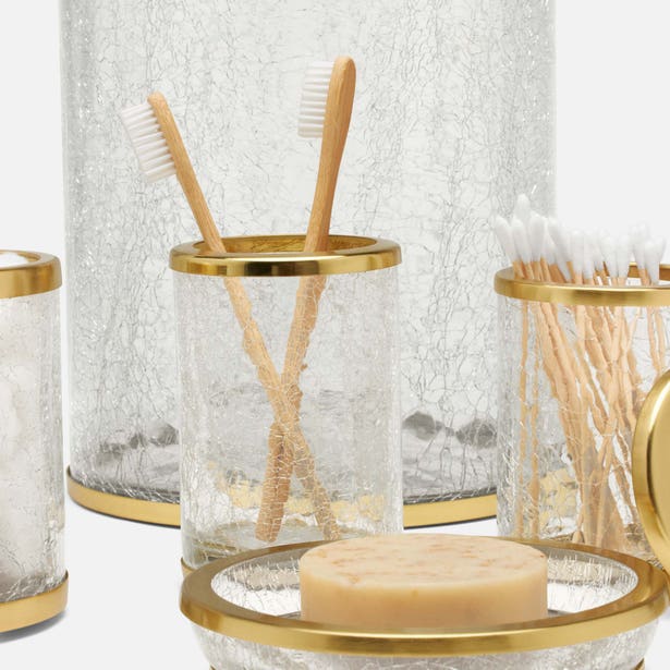 Crackle glass bath accessories with gold rims, styled with toothbrushes, cotton swabs, and soap.