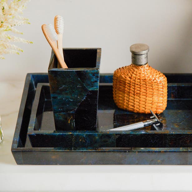 Dark blue-green stone bath tray and toothbrush holder styled with a woven bottle and razor.
