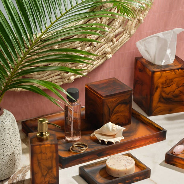 Tavira tortoiseshell resin bath accessories styled with palm leaf and seashell against blush wall.