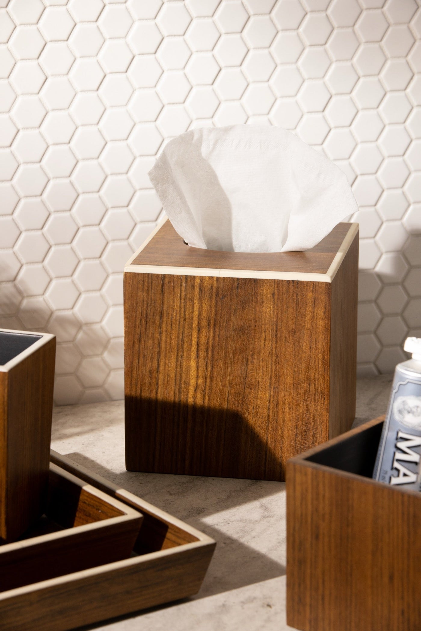 Walnut-toned wood tissue box cover with brass trim, styled on marble surface against white hex tile.