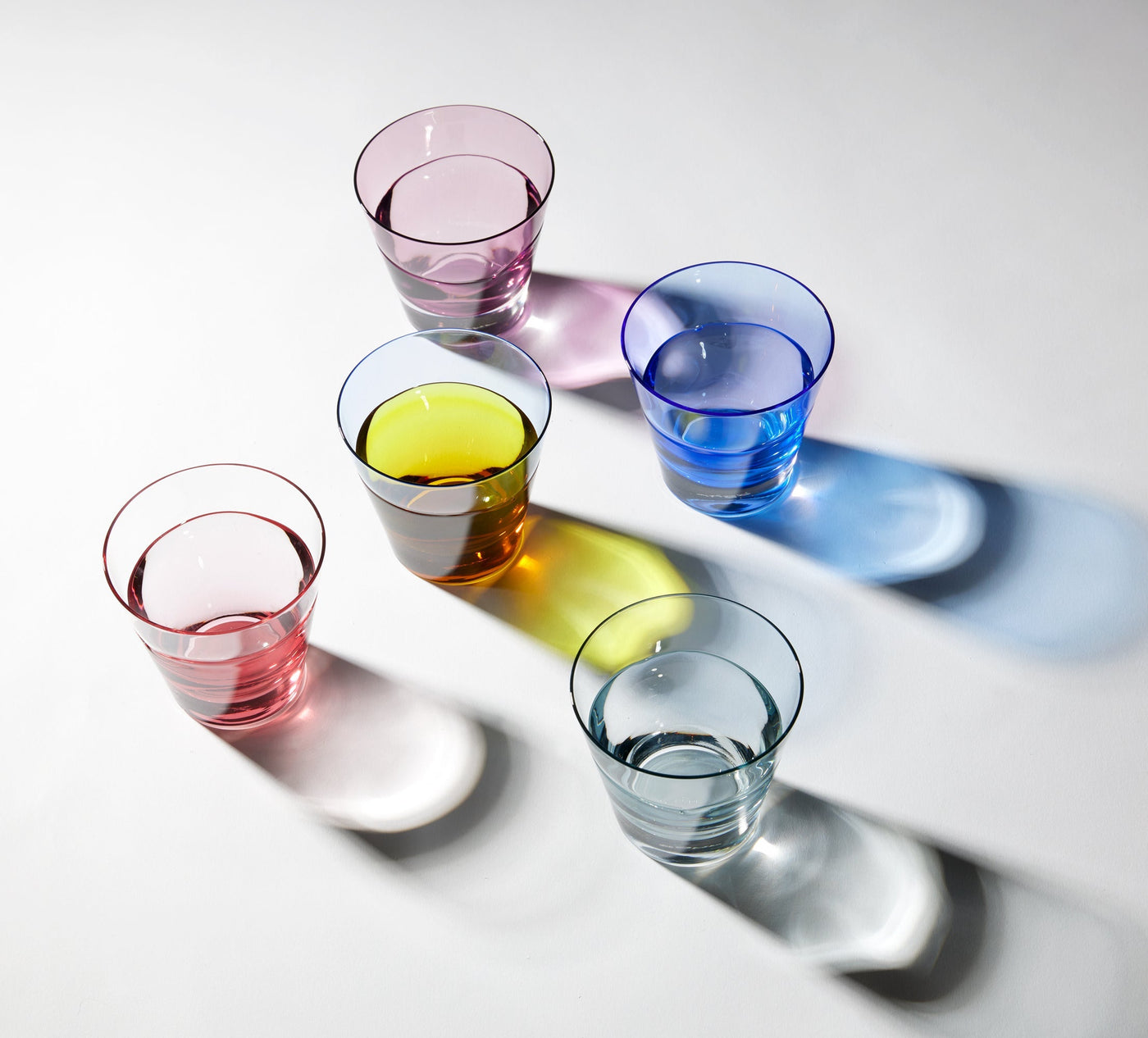 Five Sugahara Night tumblers in pink, mauve, yellow, cobalt, and ice blue casting colored shadows.