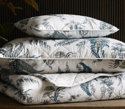 A neatly stacked set of bedding, including a pillow and two quilts, features a blue and white floral botanical print.