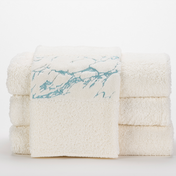 Three stacked white towels with a fourth towel draped over them, featuring a light blue marbled pattern on its border, set against a plain white background.