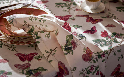 Baudin Butterfly ivory linen tablecloth with crimson butterfly and floral print, styled with dinnerware.
