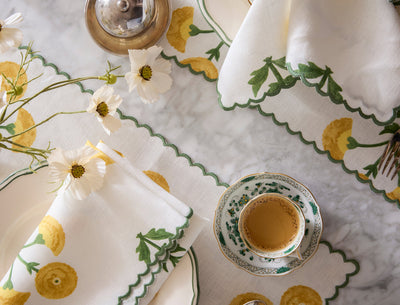 Gisele Schumacher white linen table linens with yellow floral and green scalloped edge embroidery.