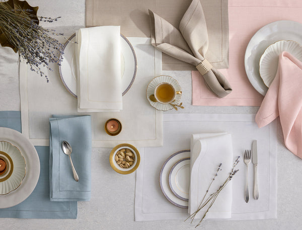 Table setting with pastel placemats, folded napkins, plates, cutlery, cups, nuts, candles, and a small bouquet of dried lavender arranged in a neat, overhead view.