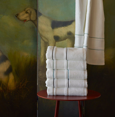 A stack of neatly folded white towels sits on a red stool; a white towel hangs above, with a painted dog in the background.