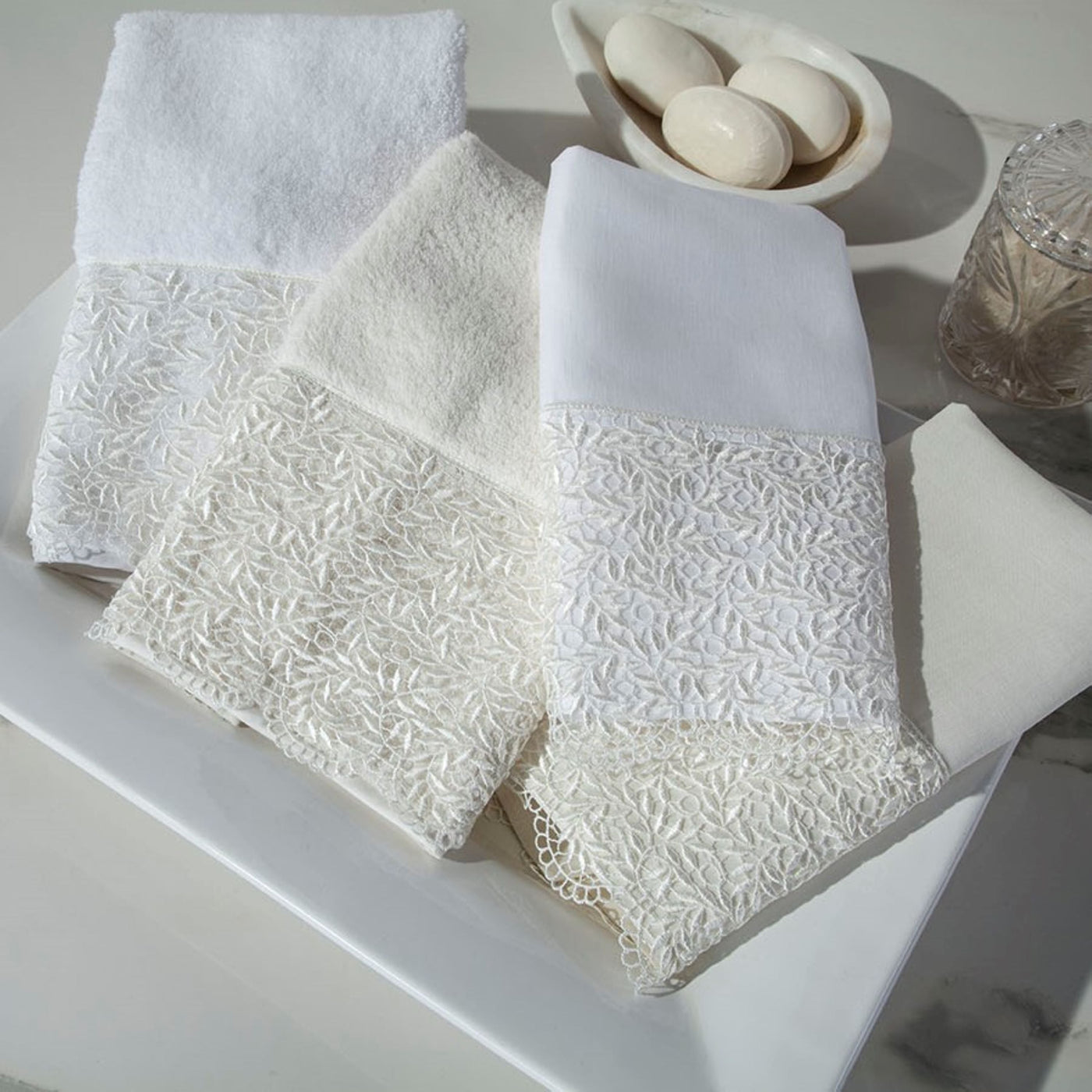 Sferra Arbor ivory cotton towels with floral lace trim, displayed on white marble surface.