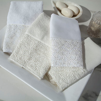Sferra Arbor ivory cotton towels with floral lace trim, displayed on white marble surface.