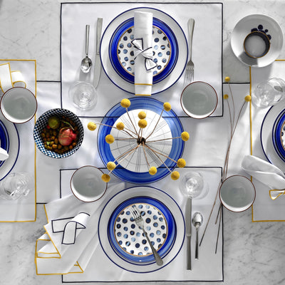 Arlo white table linens with gold border on marble table set with blue dinnerware.