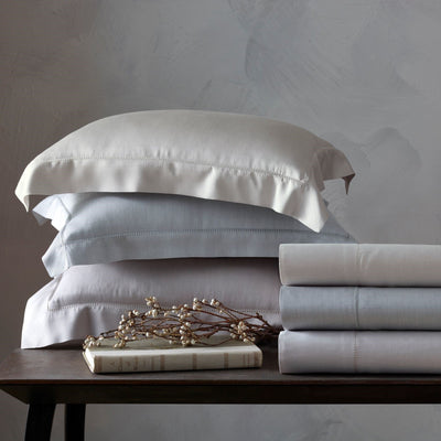 Atwood ivory and silver cotton sheet set with folded sheets and stacked pillowcases on wood table.