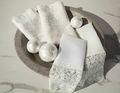 White Luzon bath linens with lace trim displayed on stone plate with decorative spheres.