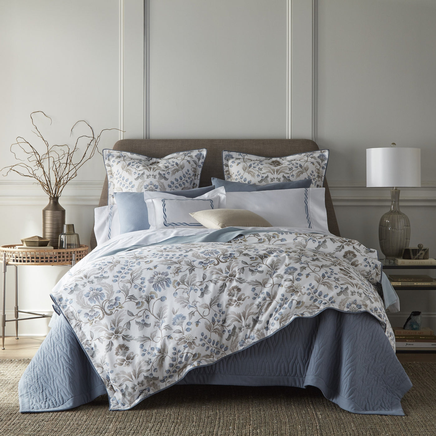 Sferra Beatrice blue and ivory floral cotton bedding styled on a bed with layered pillows.