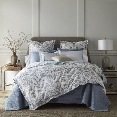 Sferra Beatrice blue and ivory floral cotton bedding styled on a bed with layered pillows.