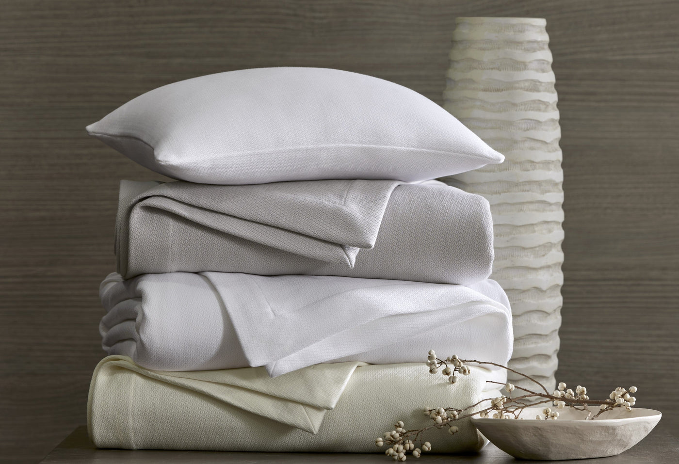 Sferra Belem white and ivory folded sheet set stacked with pillow beside textured vase.