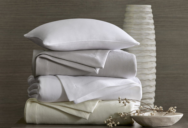 Home Treasures Belem white and ivory folded sheet set stacked with pillow beside textured vase.