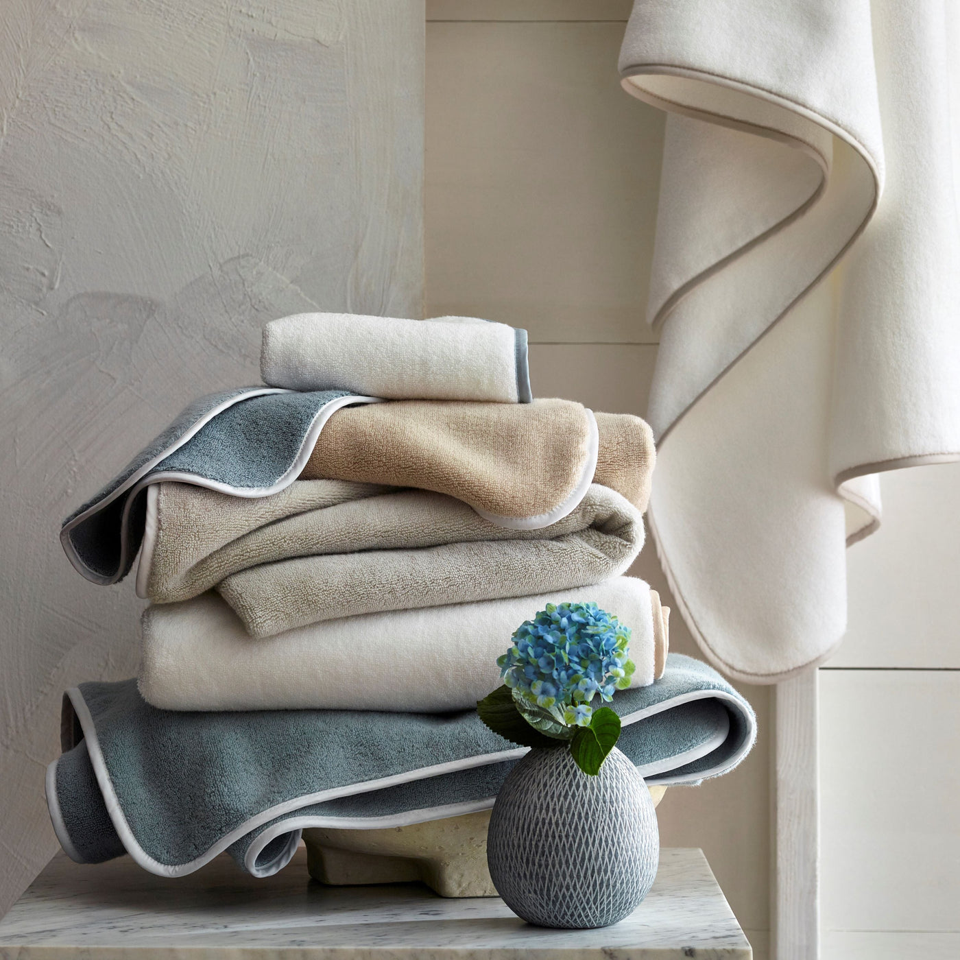 Bodrum bath towels stacked in ivory, champagne, and slate with contrast borders.