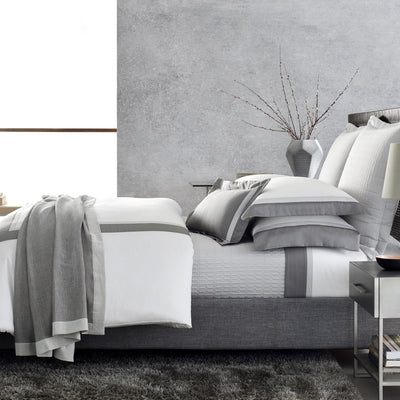 Sferra Borders white and grey cotton bedding collection on made bed.
