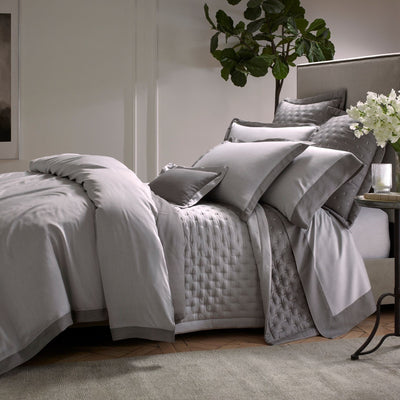 Sferra Celeste silver grey cotton bedding collection styled on a bed with quilted coverlet.