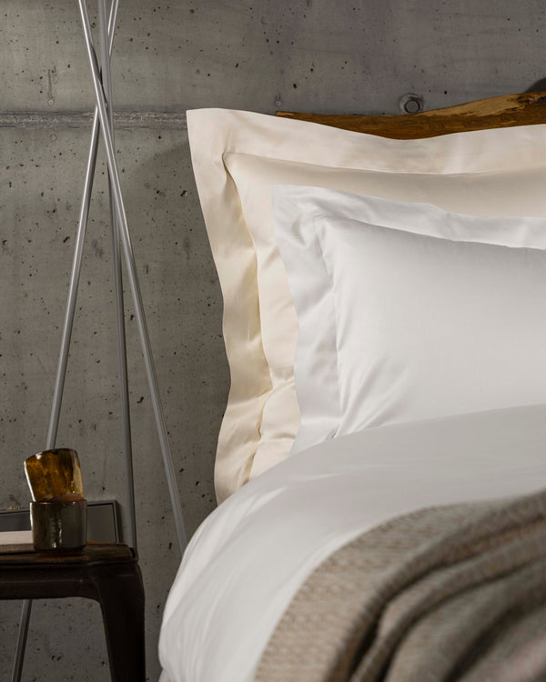 A close-up view of a bed with cream-colored sheets and several white and beige pillows arranged against the headboard.