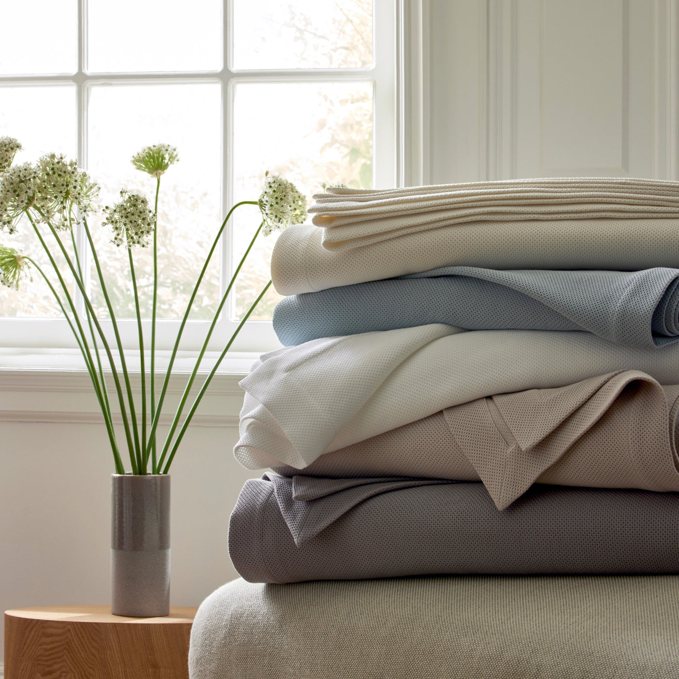 Comporta bedding collection stacked in ivory, mist blue, sage, taupe, and slate hues.
