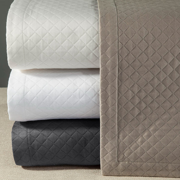 Home Treasures Diamante quilted coverlets stacked in ivory, white, charcoal, and taupe.