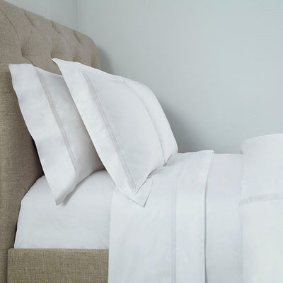 Sferra Doric white cotton bedding with silver embroidered border on linen headboard bed.