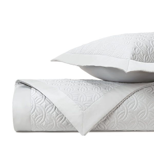 Duomo white quilted coverlet and sham with geometric embroidered pattern, neatly folded.