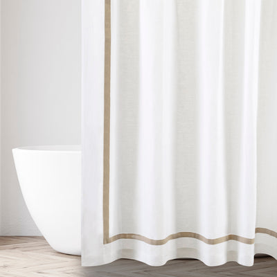 Fino white shower curtain with tan border trim, hanging beside a freestanding bathtub.