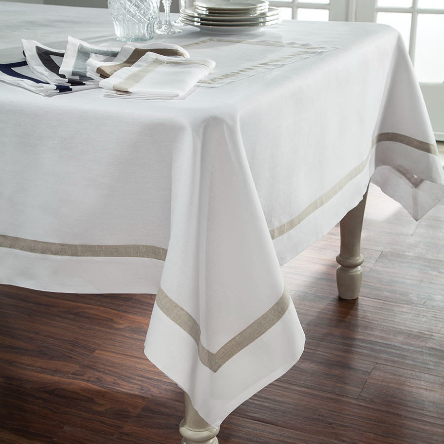 Fino white linen tablecloth with champagne border trim on a dining table.