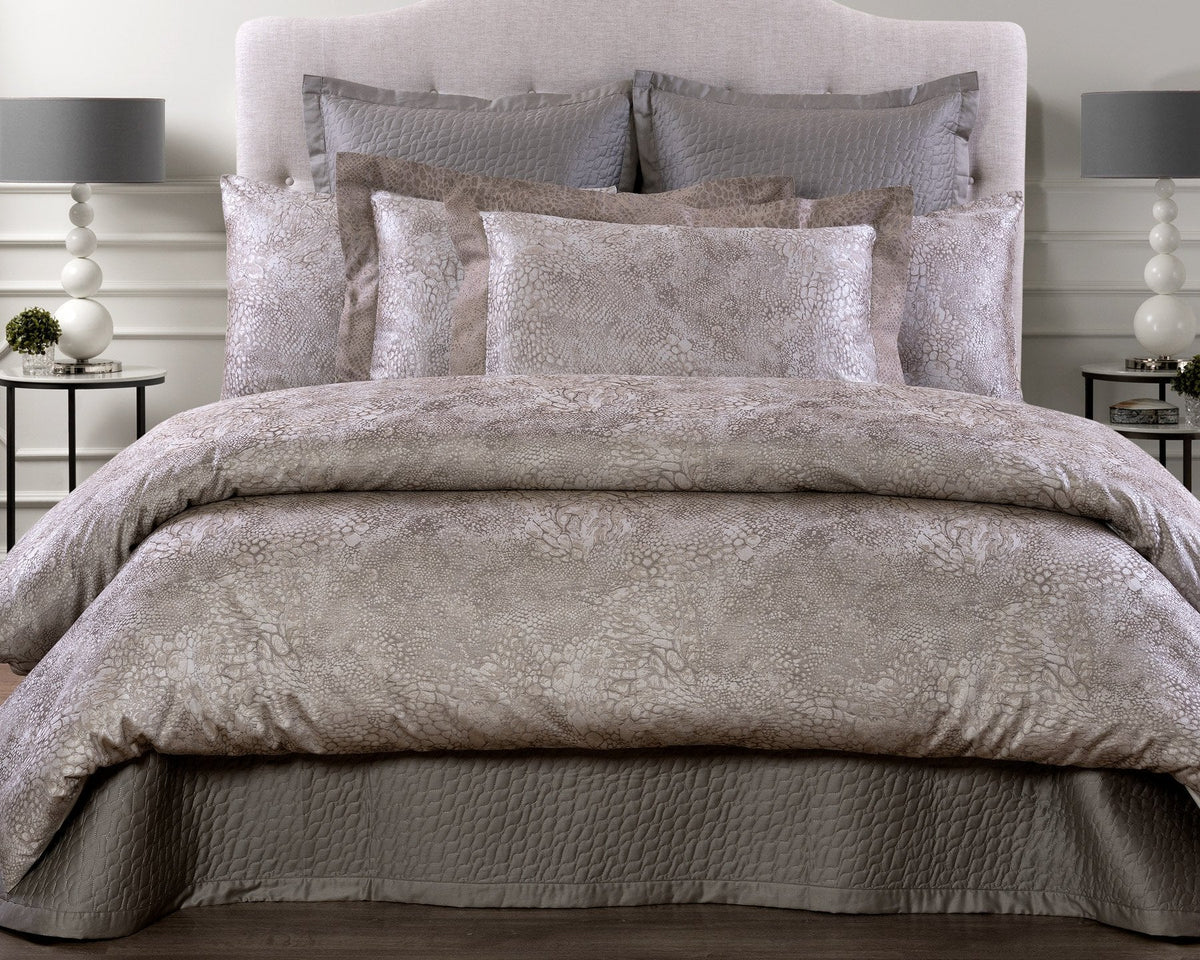 Bed dressed in taupe and pale grey Ibla jacquard duvet cover and shams, with a quilted taupe coverlet at the foot.