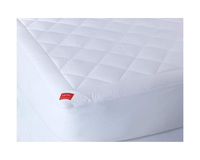 Close-up of a white quilted mattress protector with a red label on one corner, fitted over a mattress.