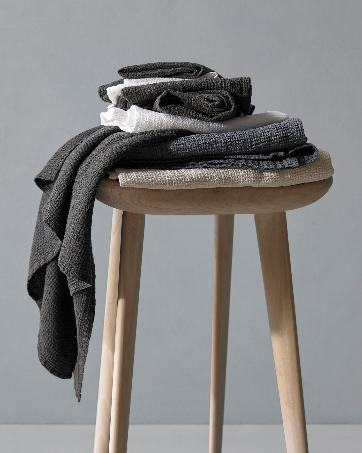 Lipe linen waffle bath towels in charcoal and natural stacked on a wooden stool.