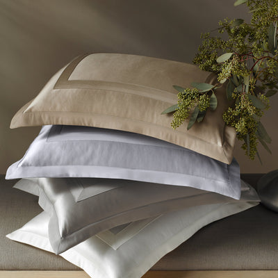 Sferra Lustro pillowcases stacked in champagne, silver, and white sateen cotton.