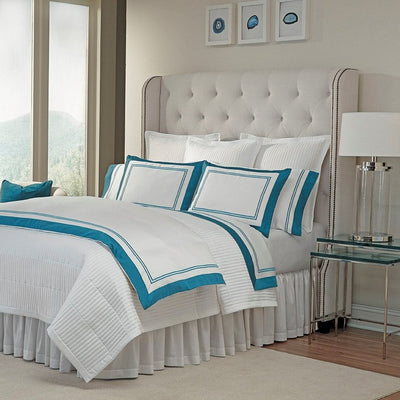 Sferra Marco white bedding collection with teal border on bed with tufted headboard.