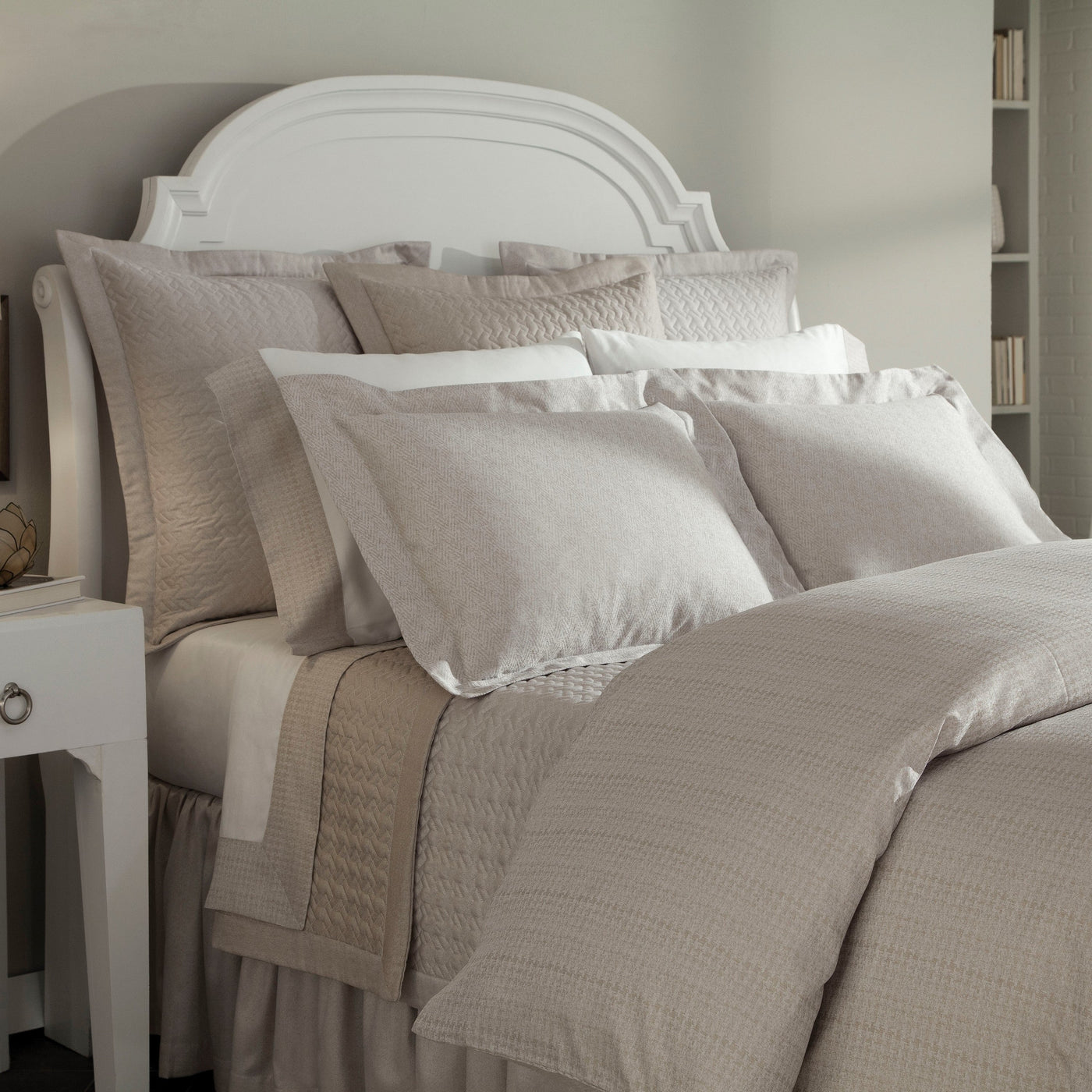 Mayfair bedding collection in champagne linen on styled bed with white arched headboard.