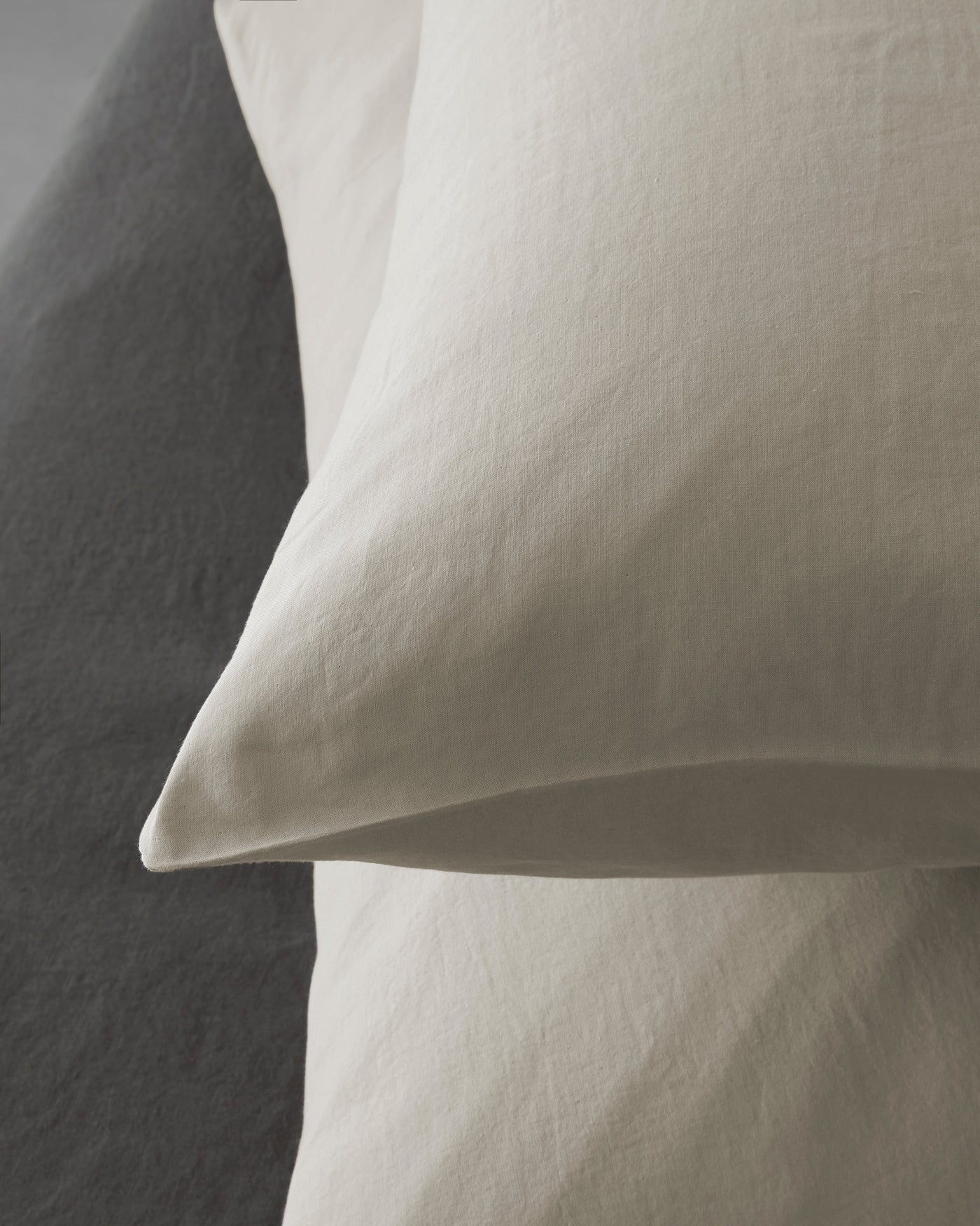 Two ivory cotton voile pillowcases stacked against a charcoal linen backdrop.