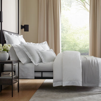 Sferra Giza 45 white cotton bedding collection styled on a bed in a neutral bedroom.