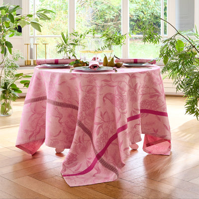 À L'Orangerie rose jacquard tablecloth on round dining table with green plants.