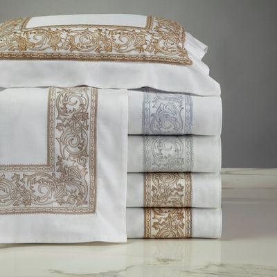 Sferra Paris white cotton sheets stacked with gold and silver baroque embroidered borders.