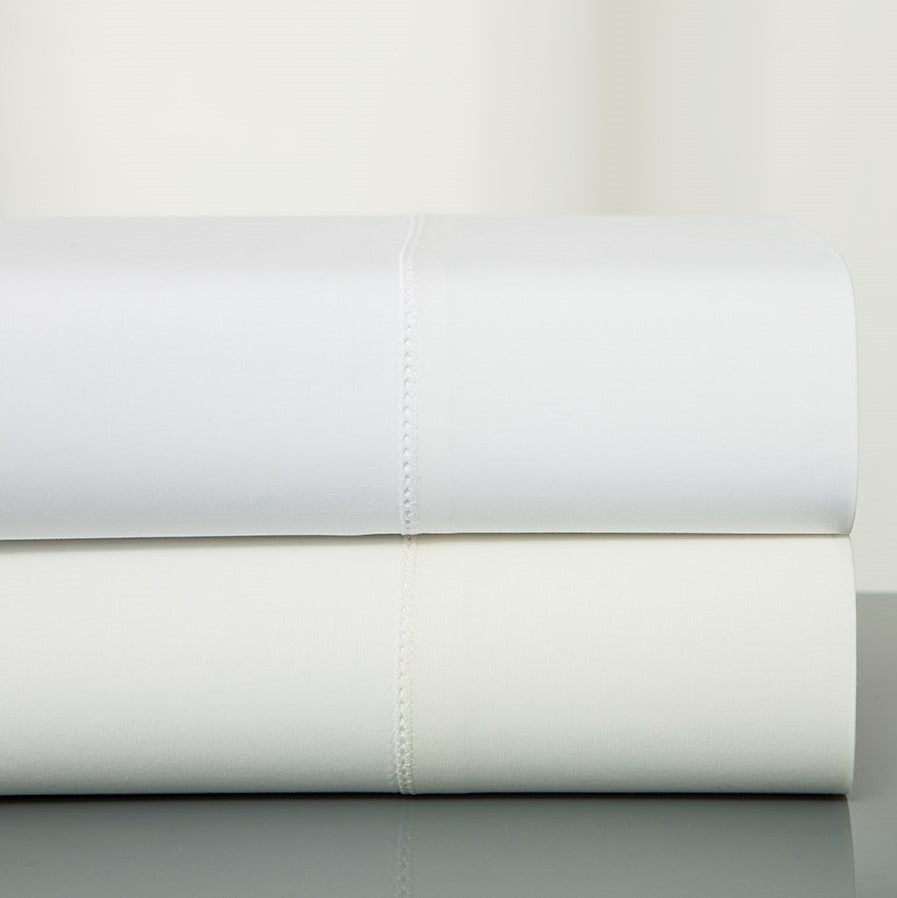 Polycotton folded flat sheets stacked in white and ivory with hemstitch detail.