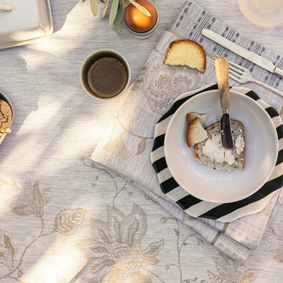 Floral Beige table linens by le jacquard with dishes and food, on a sunny day.