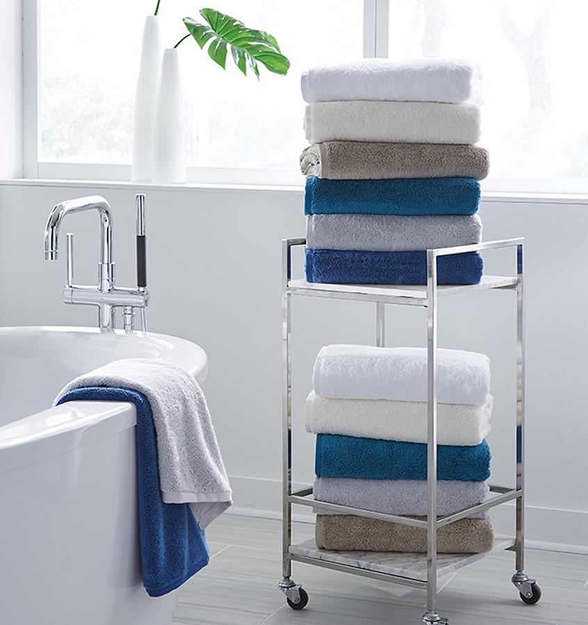 Sferra Sarma bath towels in white, teal, and taupe stacked on chrome cart.