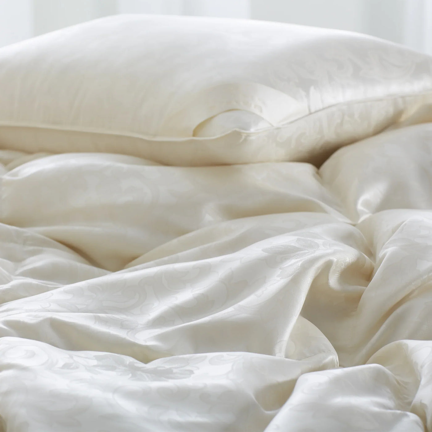 St. Petersburg ivory silk-finish down bedding with pillow, softly draped on bed.