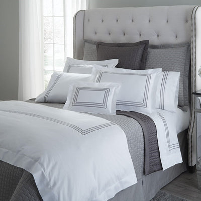 Sferra Stella white bedding with charcoal embroidered border on styled bed.